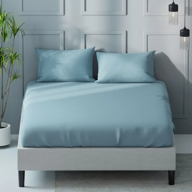 Front view of a blue solid bedsheet and two pillows on a king-size bed