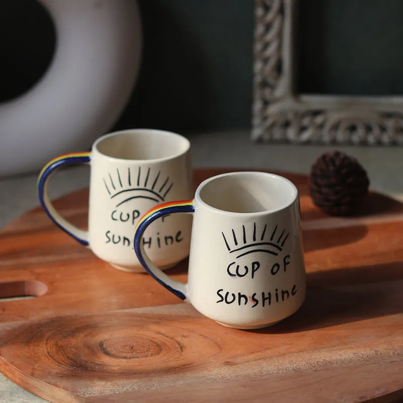 Two white sunshine mugs with colourful handles arranged on a wooden table
