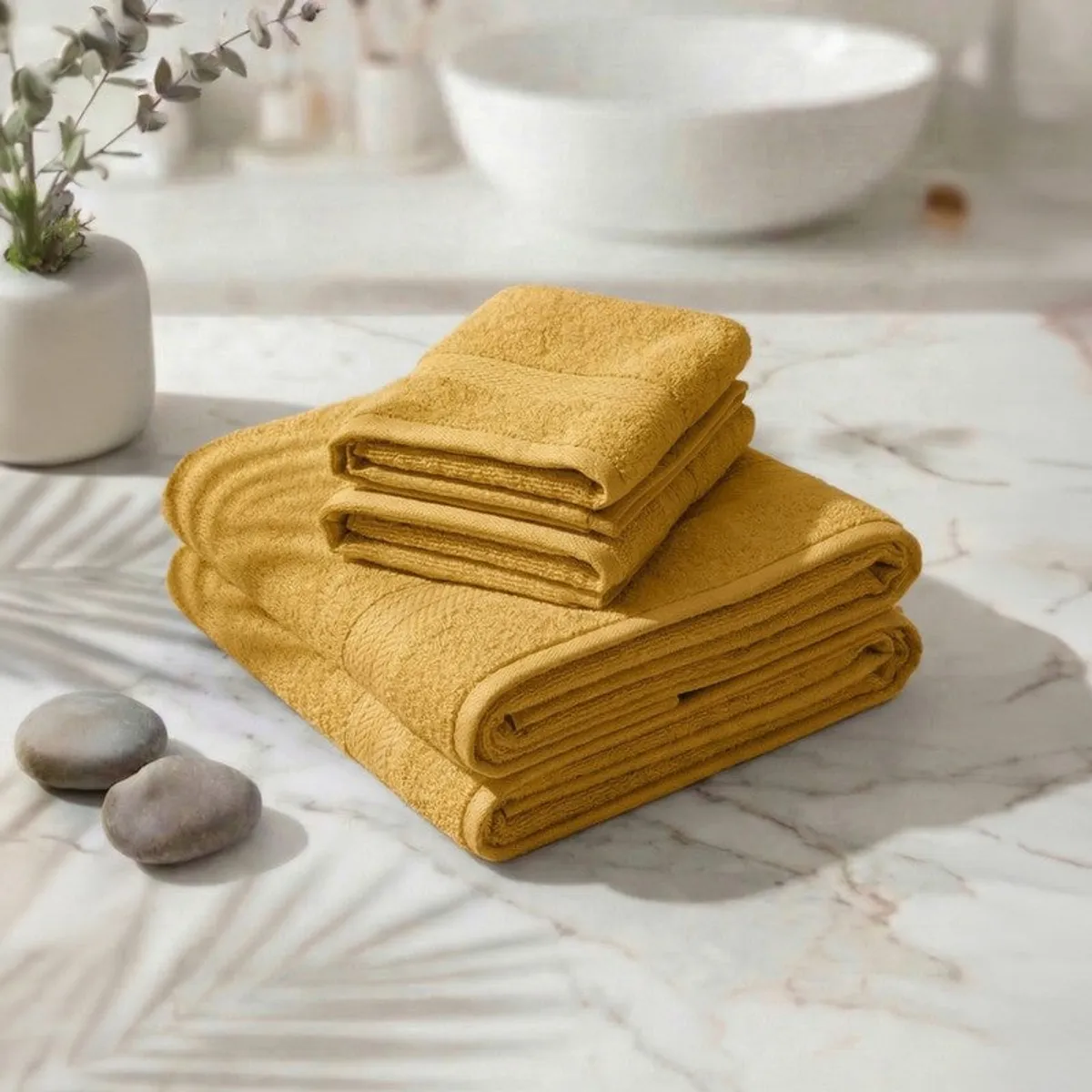 Folded yellow towel set arranged on a marble surface in a bathroom setting.