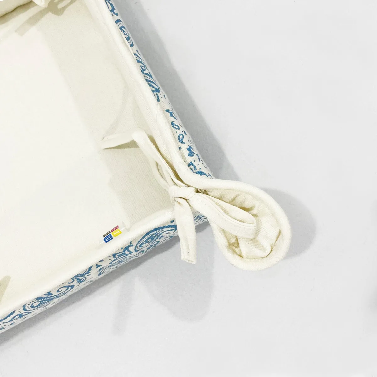 Close-up of cream cotton bread basket corner with tied bow and blue printed edge