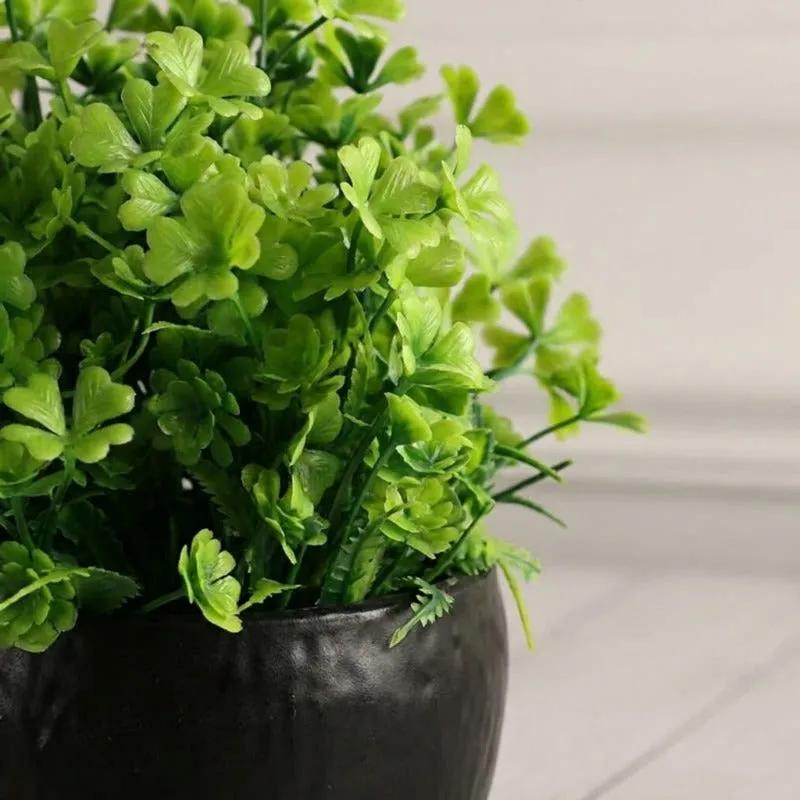Close-up of green faux leaves and the black pot with a subtly textured finish.