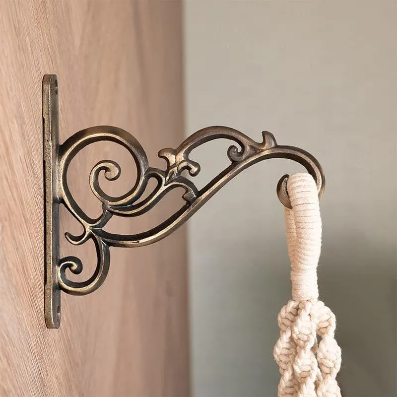 Copper scrollwork wall bracket mounted on wood with a hanging macramé piece