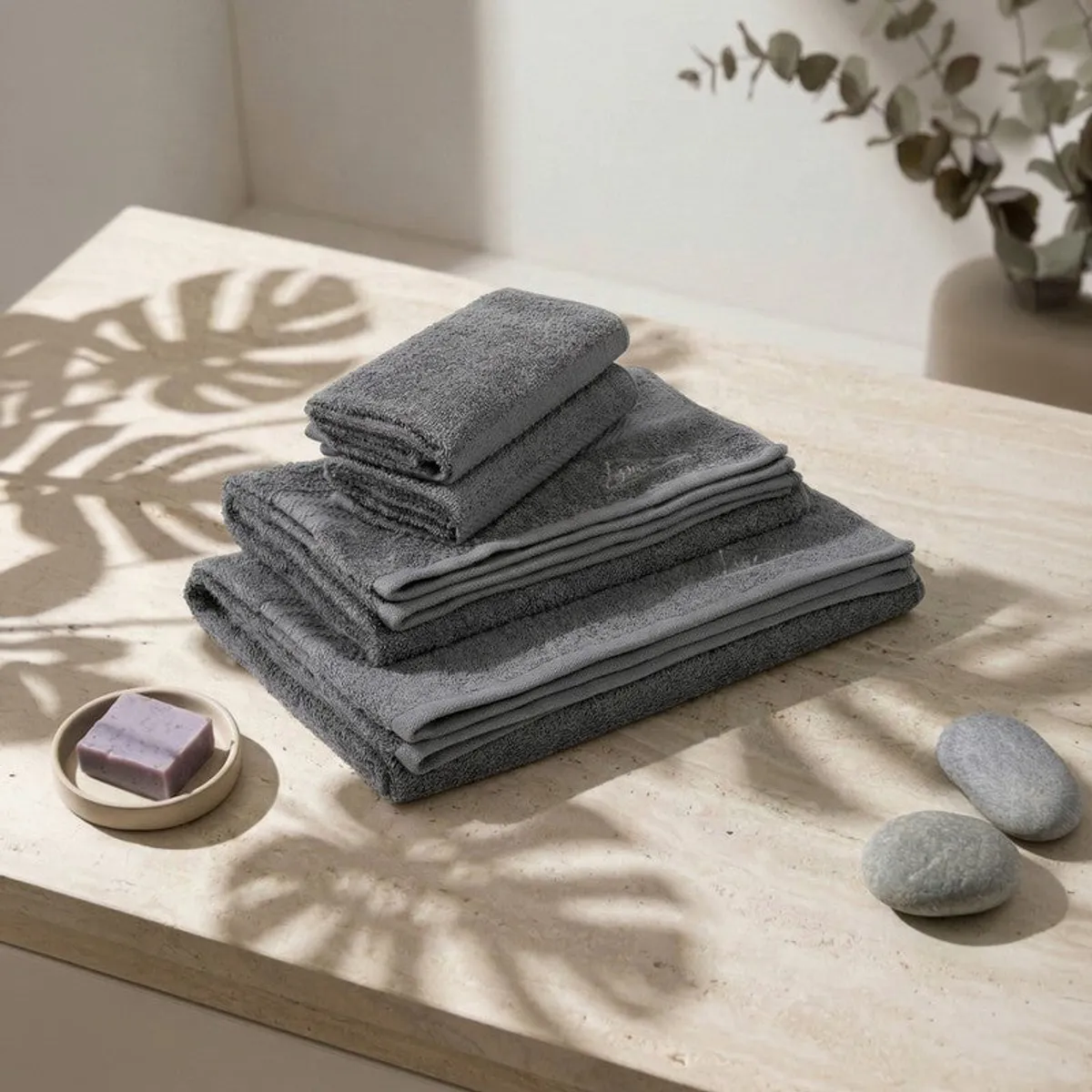 Stack of dark grey towels on a stone surface with soap and pebbles