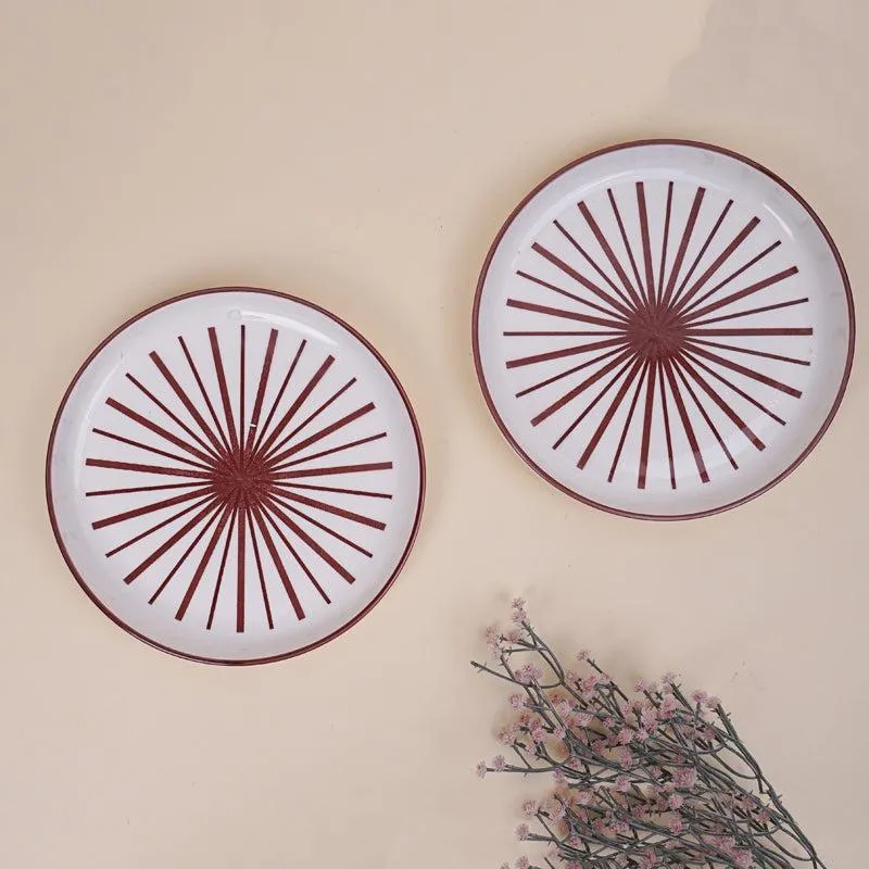 Two white snack plates with maroon starburst pattern on a beige background