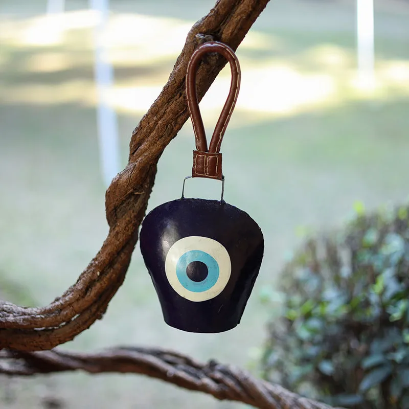 Eye-motif metal bell hanging from a tree branch outdoors