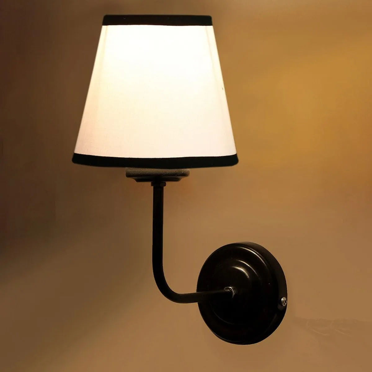 Close-up of lit white shade wall lamp with black trim and round base