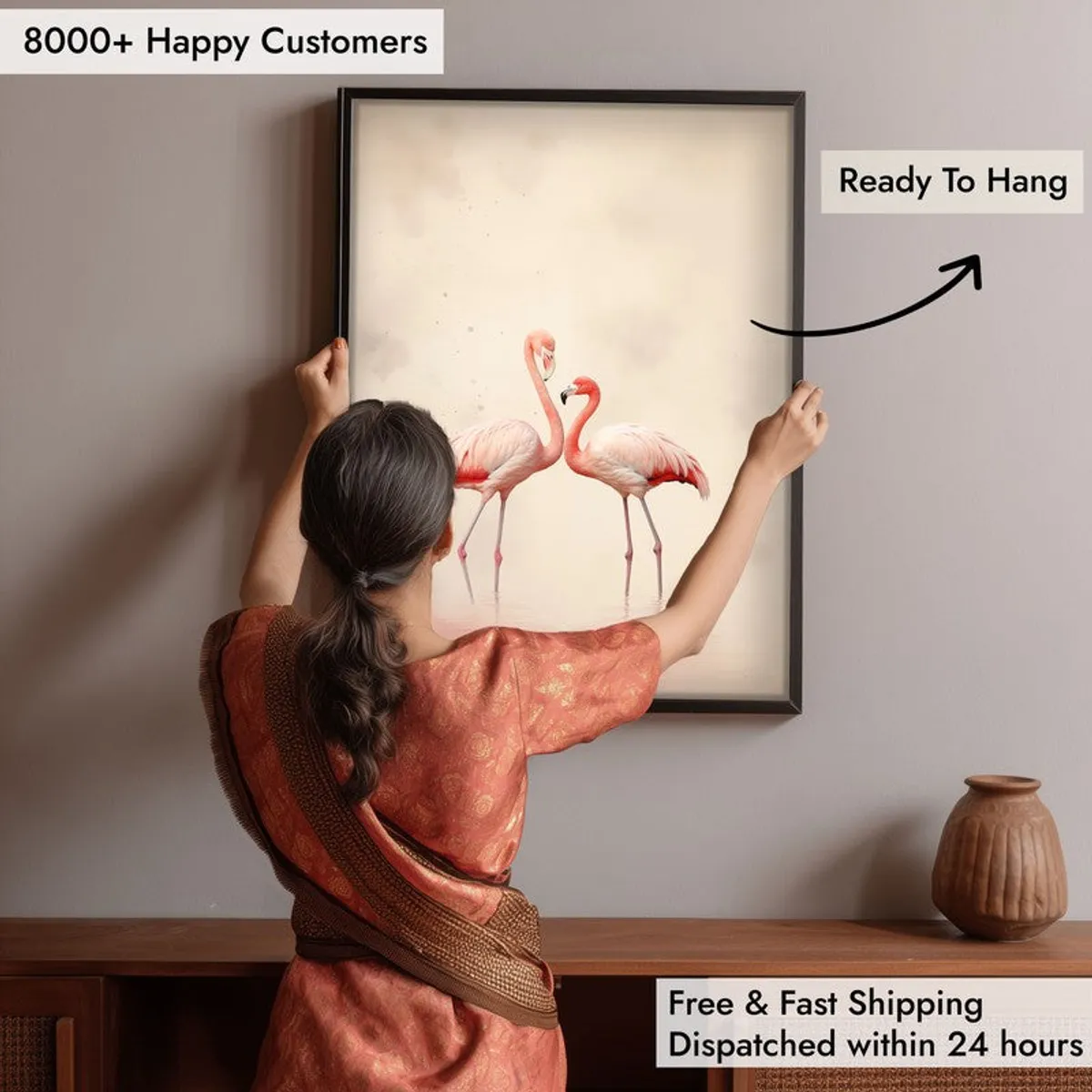 Woman hanging framed flamingo wall art above a wooden console