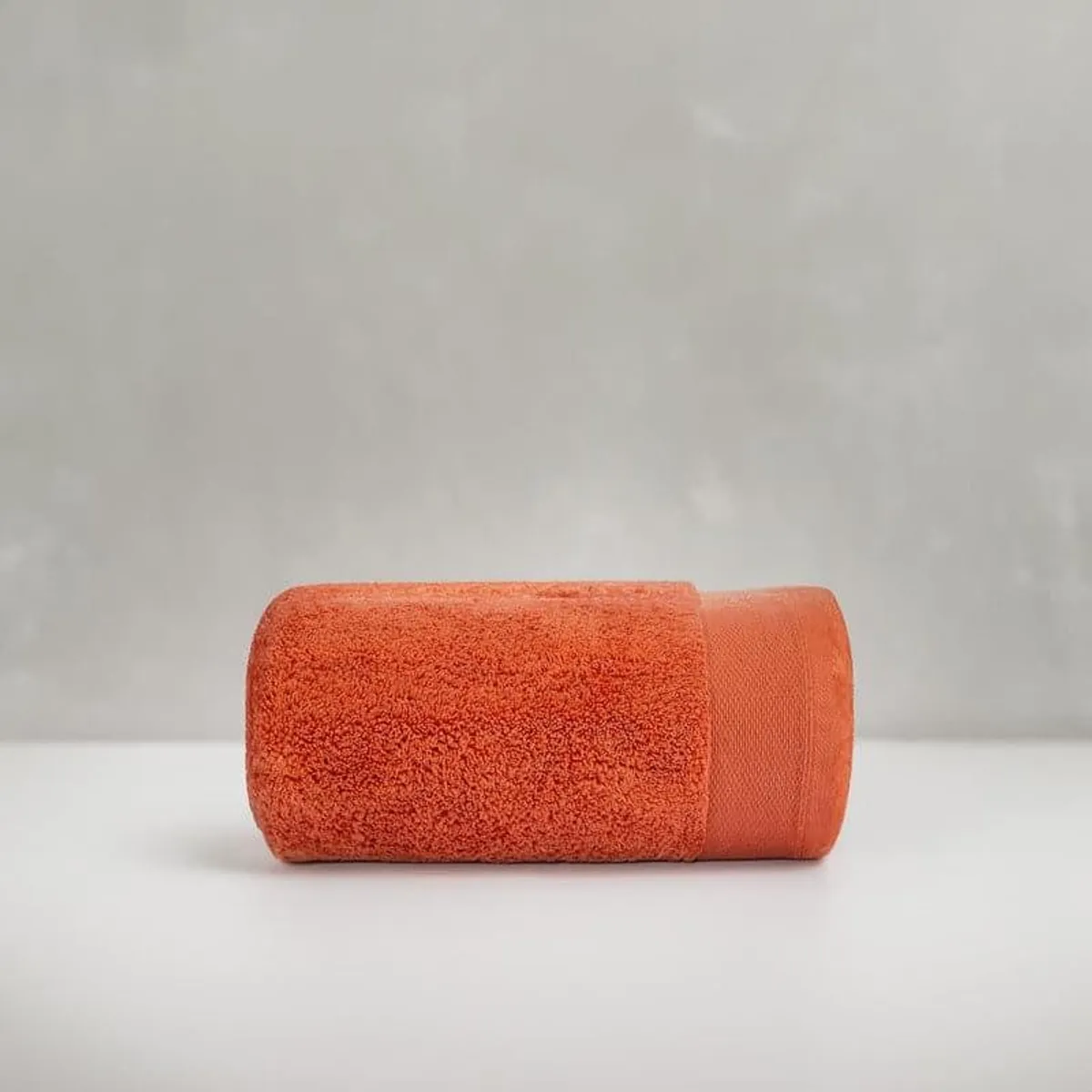 Rolled orange bath towel shown against a neutral background