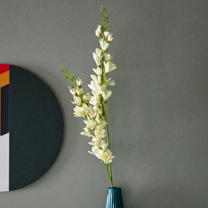 Tall artificial flower stick with white blossoms and green stem in a blue vase