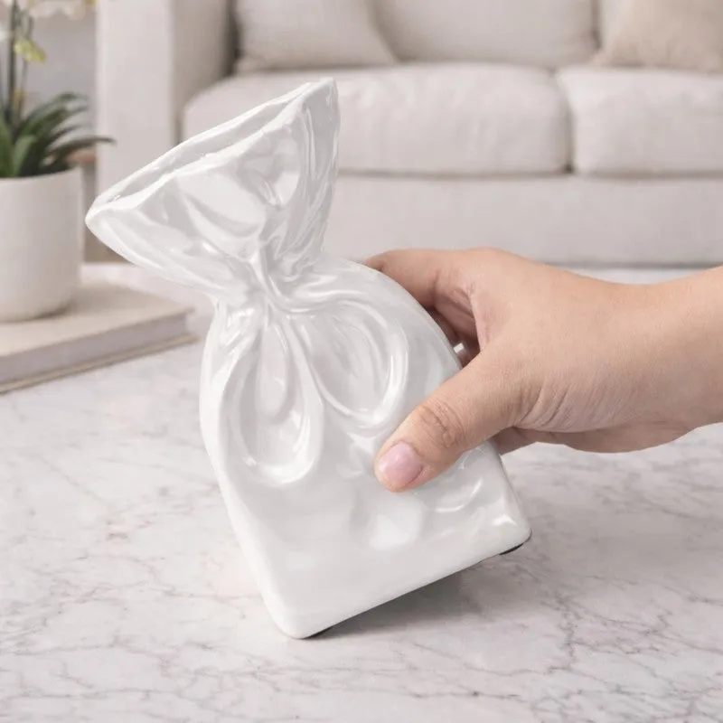 Hand holding a glossy white sculptural vase over a marble tabletop