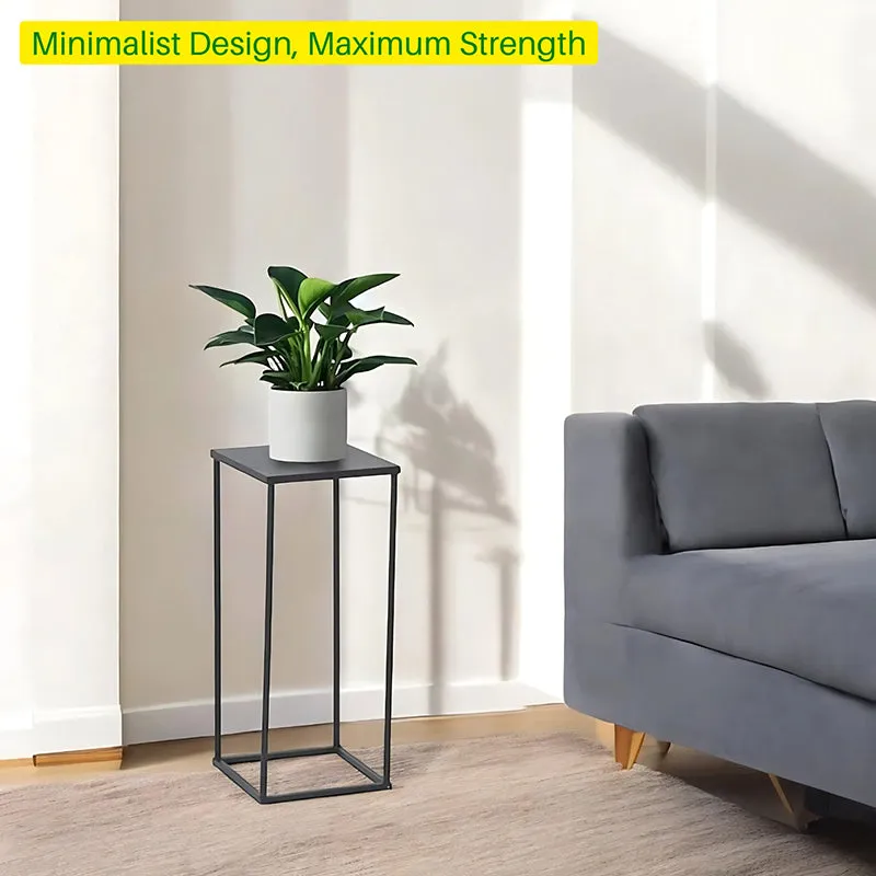 Black minimalist planter stand with a white pot beside a grey sofa.