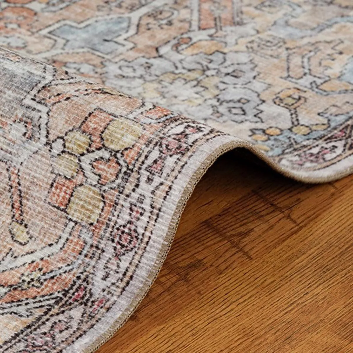 Curled corner of the flat-pile patterned carpet on wooden flooring