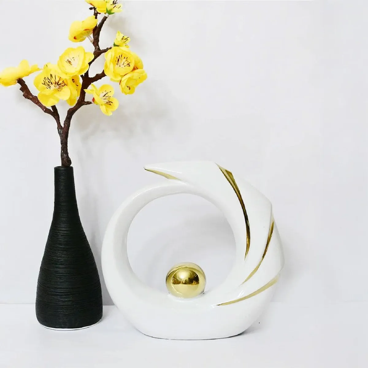 White and gold curved ceramic showpiece beside a black vase with yellow flowers
