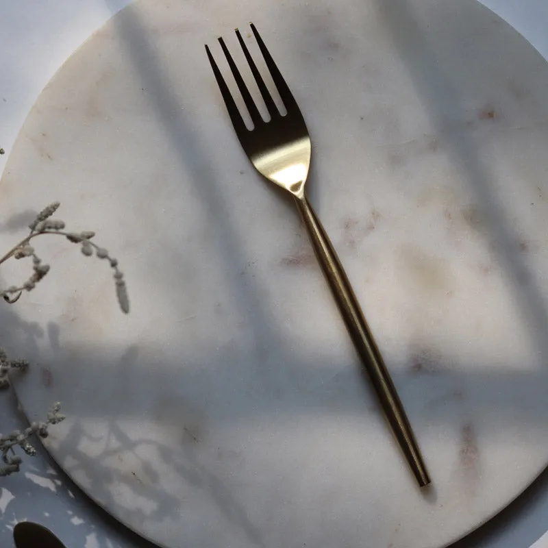 Gold fork with a slim handle placed on a round white surface