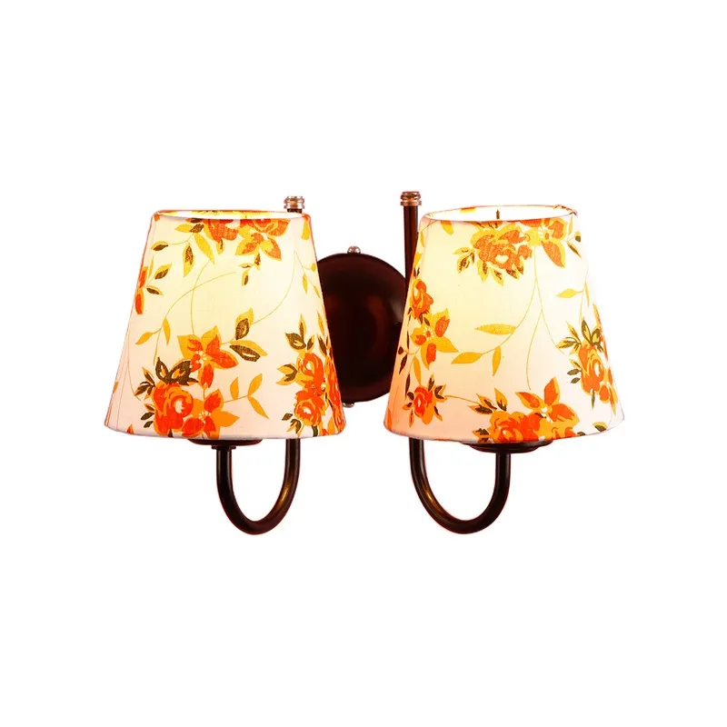 Lit orange and white floral twin-shade wall lamp on a white background