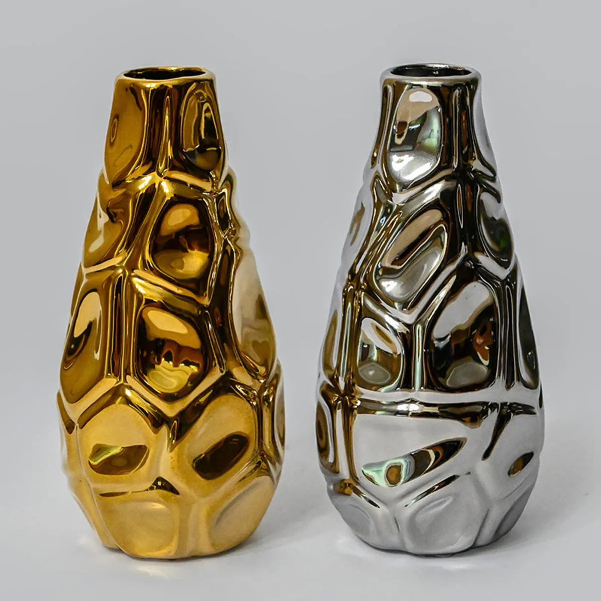Gold and silver sculptural vases side by side on a plain background