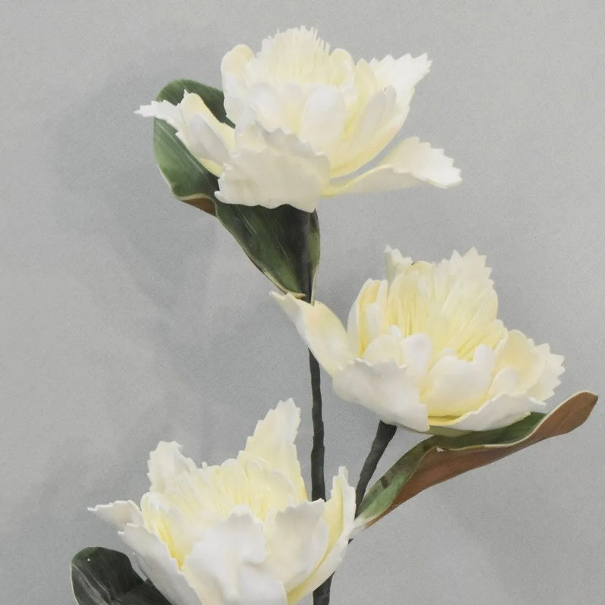 Close-up of three white artificial dahlia flowers and green leaves