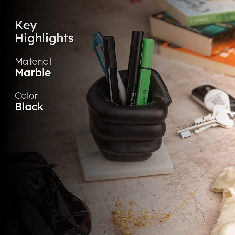 Black fist-shaped pen stand with pens on white marble base