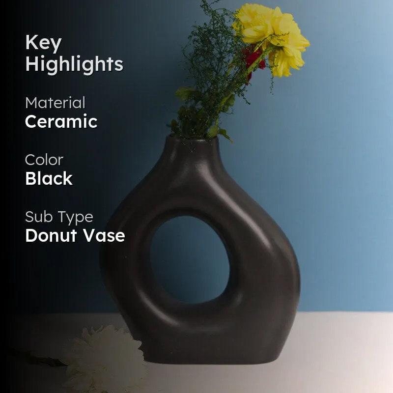 Black donut-shaped vase with flowers against a blue background