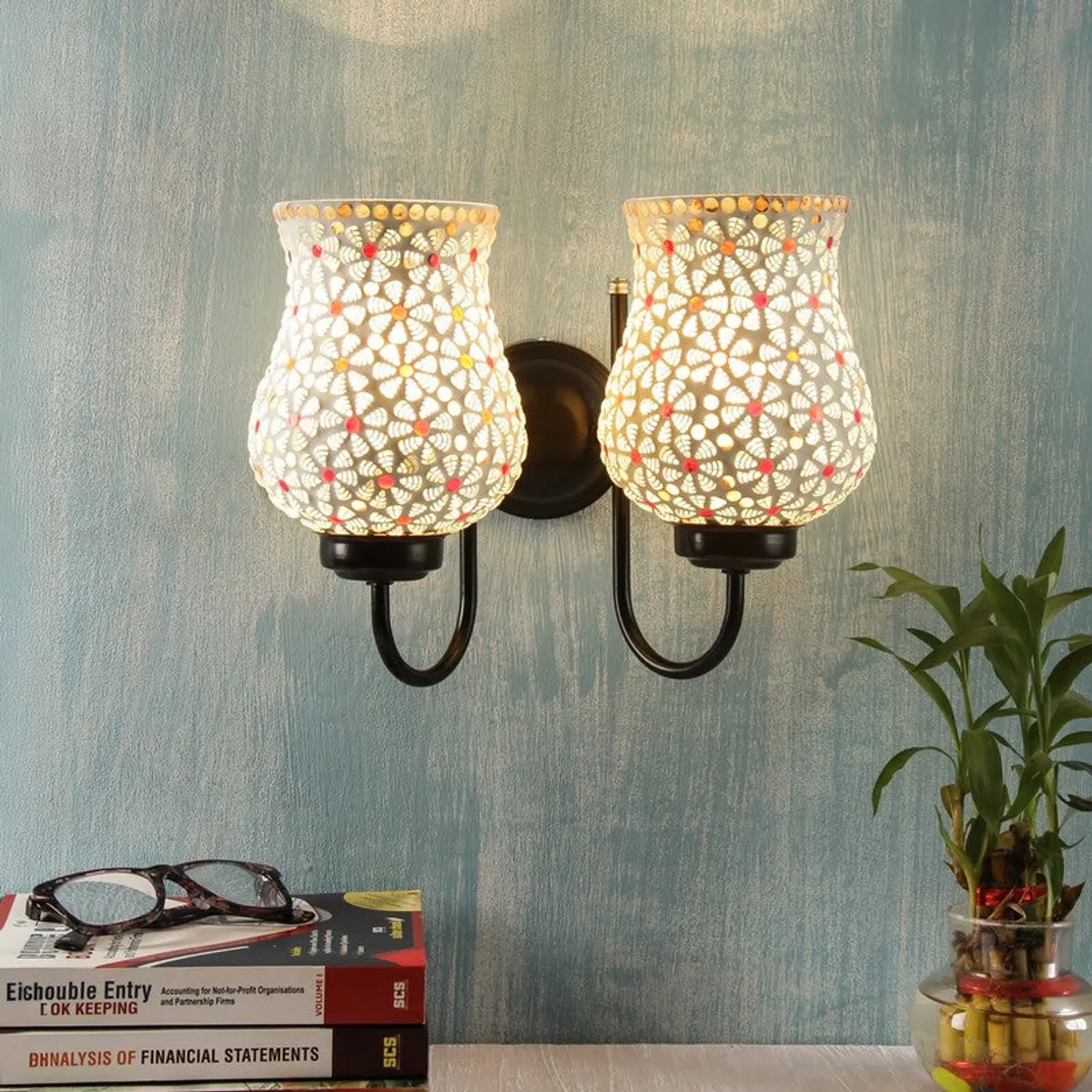 White dual wall lamp with floral cutwork glass shades on a blue wall