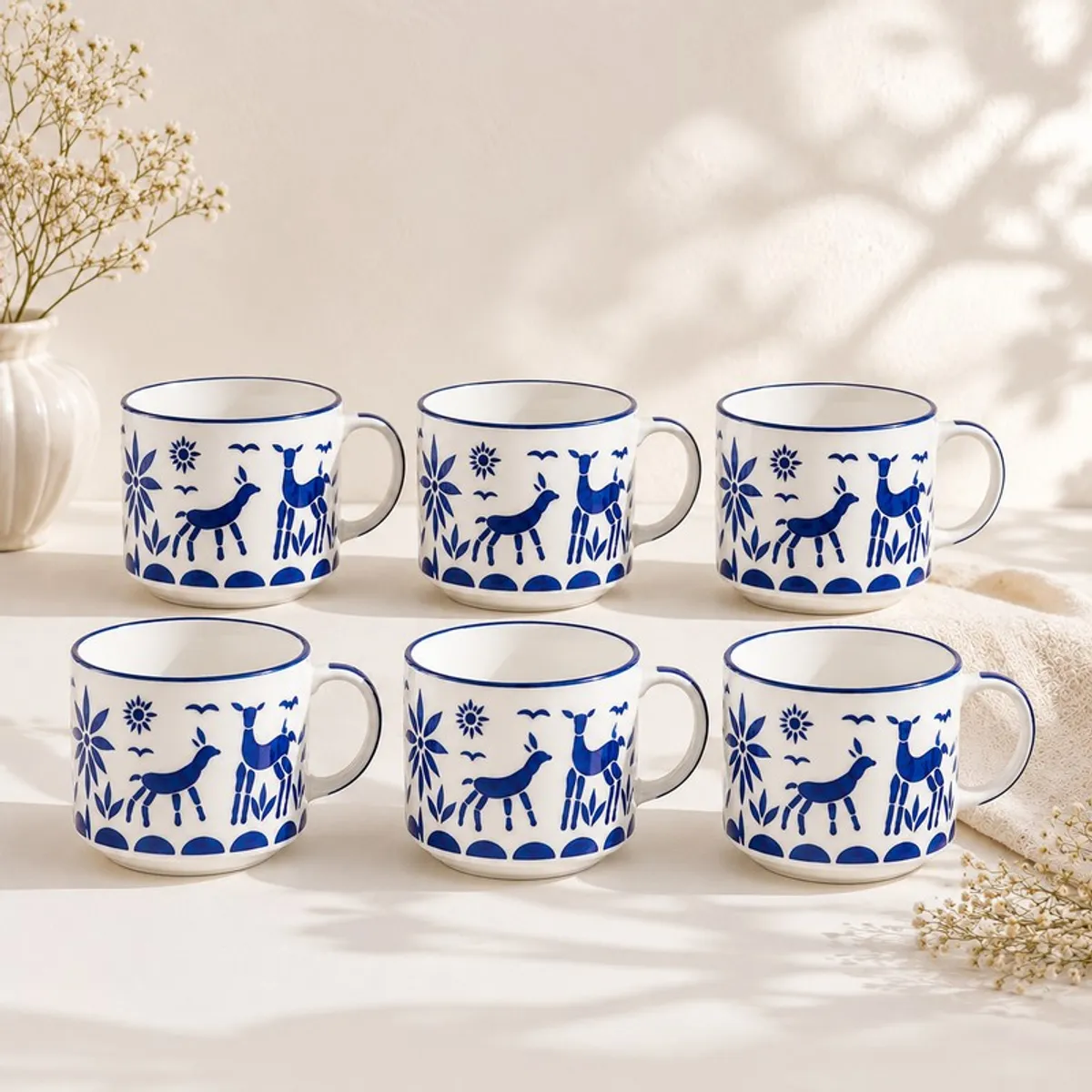 Six matching white cups with blue reindeer and floral designs displayed in two rows.