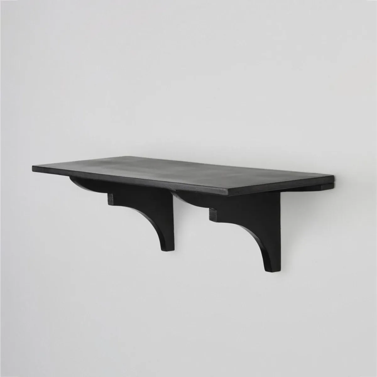 Angled view of a black wooden wall shelf with curved support brackets