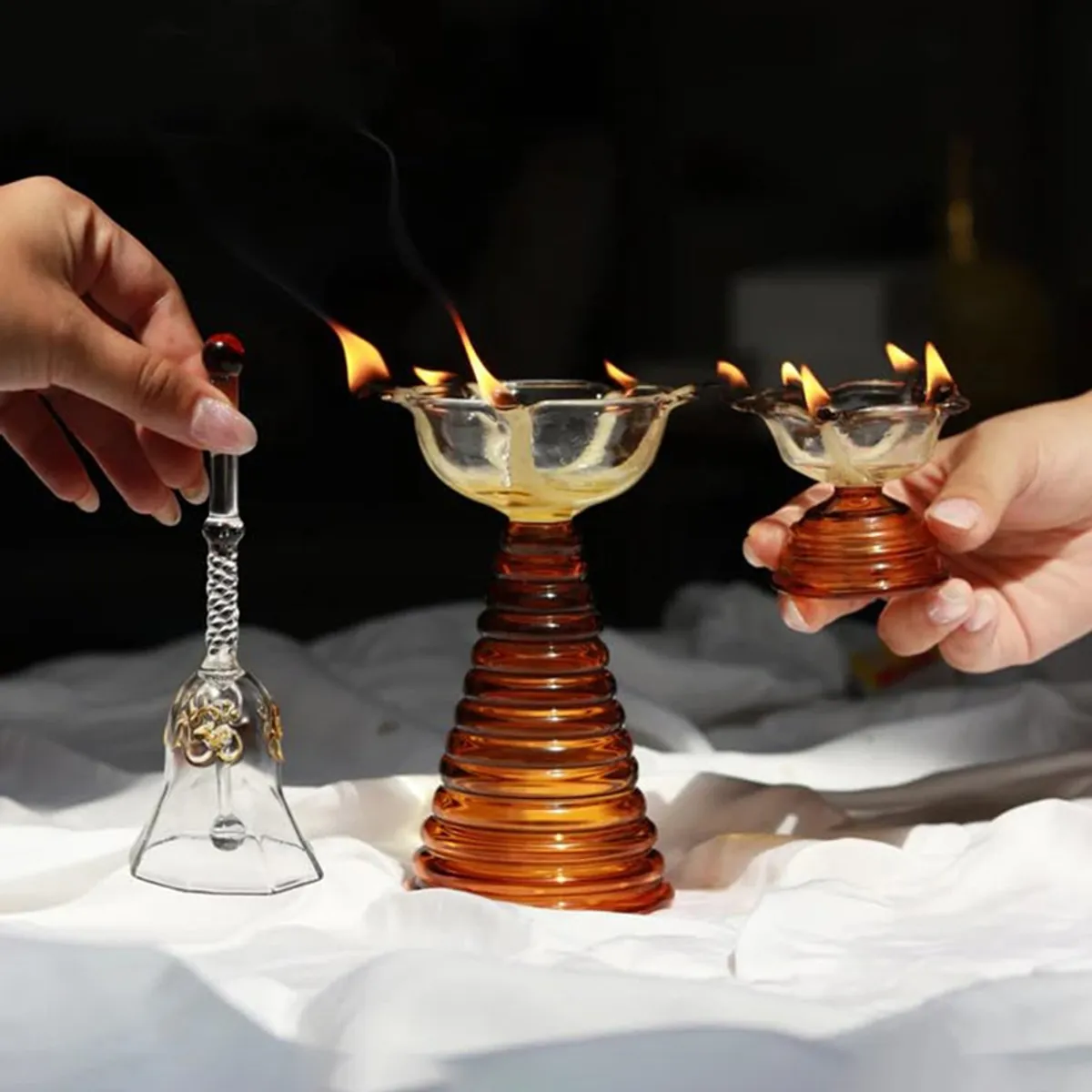 Glass pooja bell and two diyas shown with lit flames