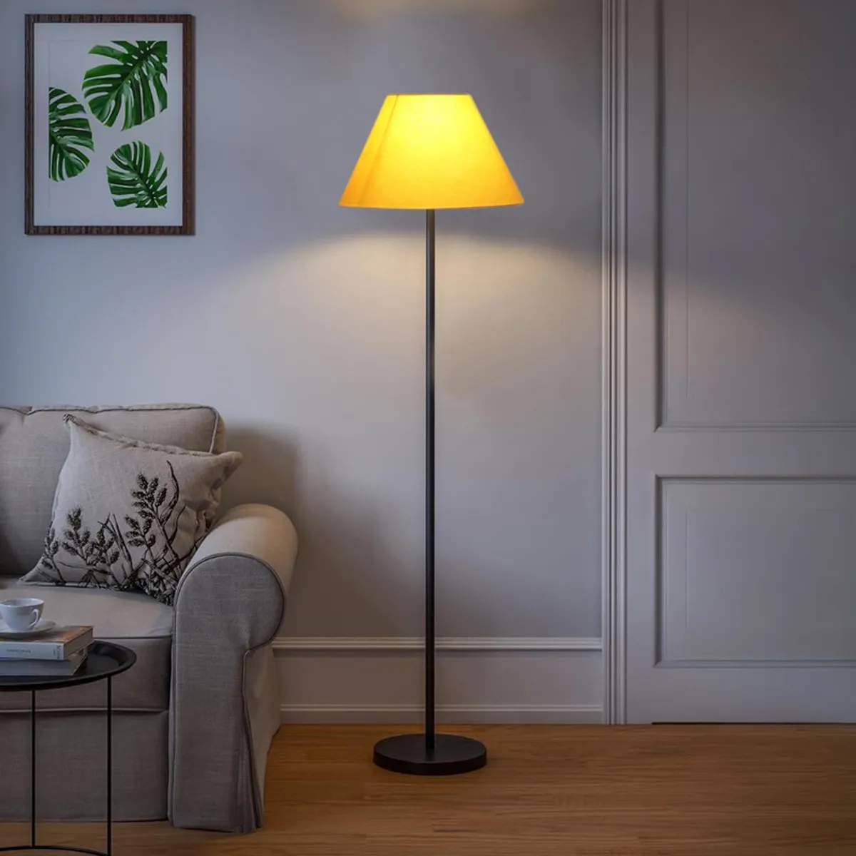 Yellow shade floor lamp lit beside a sofa in a softly lit room
