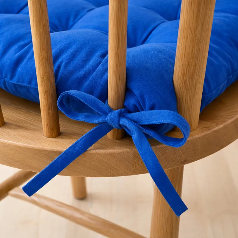 Close-up of a blue chair pad secured to a wooden chair with tie straps.