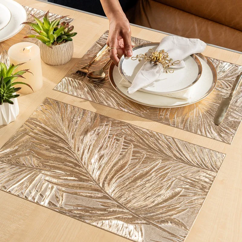 Hand placing a plate on metallic palm leaf table mats on a dining table