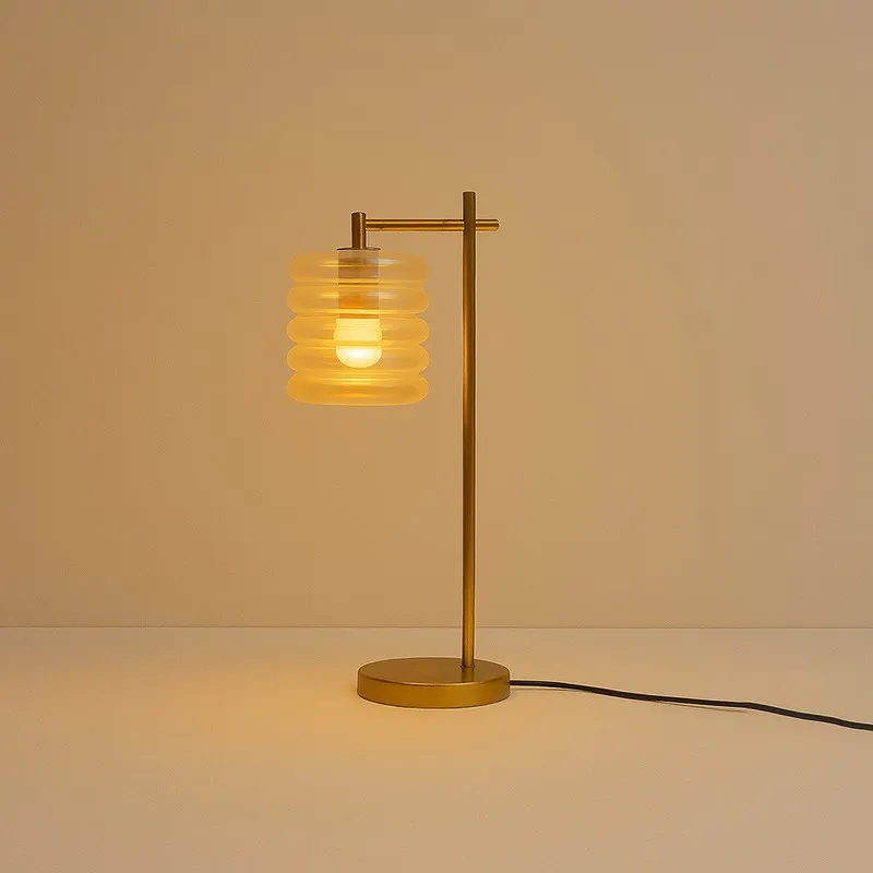 Lit transparent ribbed glass table lamp with gold-toned stand and visible cord