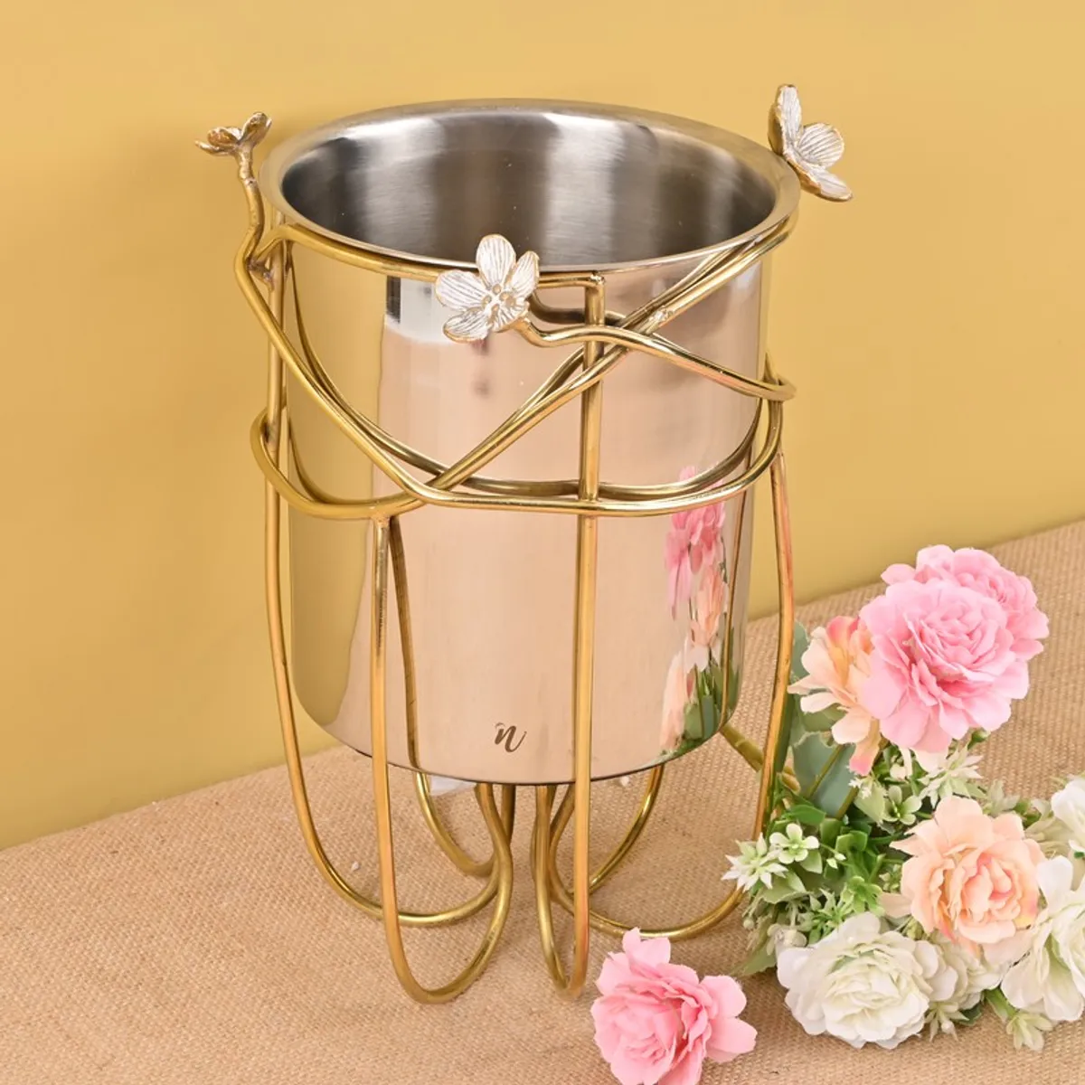Glossy ice bucket with gold floral stand displayed beside pink flowers