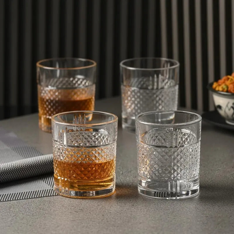 Four clear textured whiskey glasses, two filled with amber drink