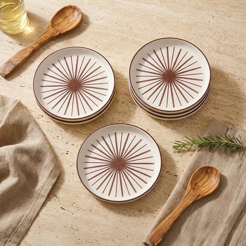 Stacked white quarter plates with maroon starburst design on a beige tabletop