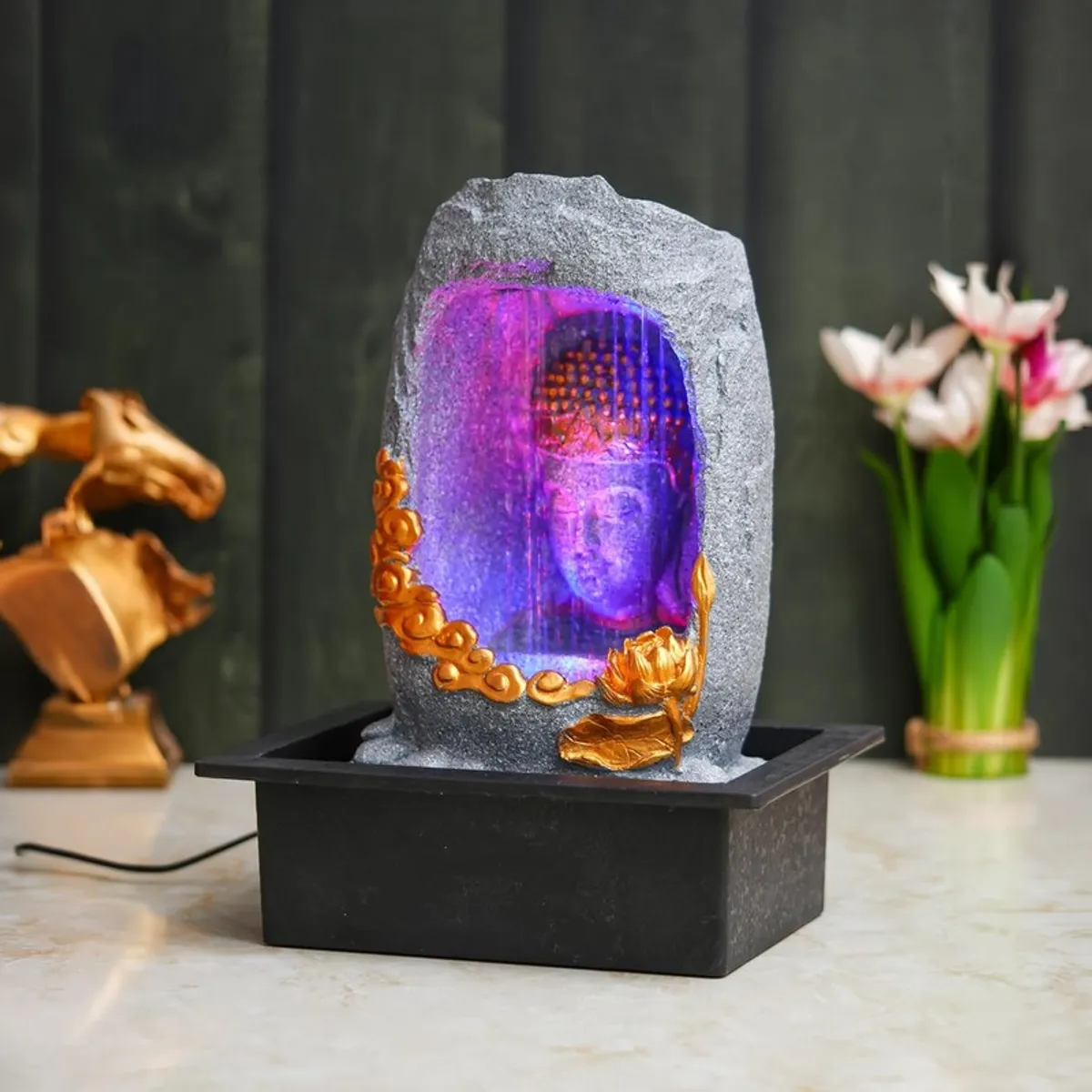 Angled view of grey Buddha fountain with purple LED water flow