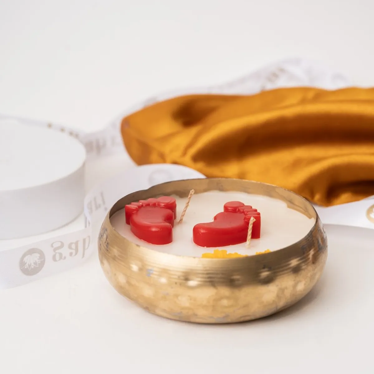 Close view of a round metal candle with red footsteps and yellow floral accents.