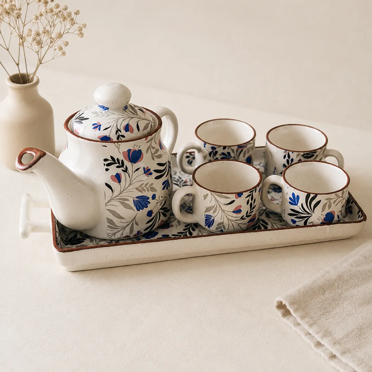 Ceramic tea pot and four floral cups arranged on a serving tray