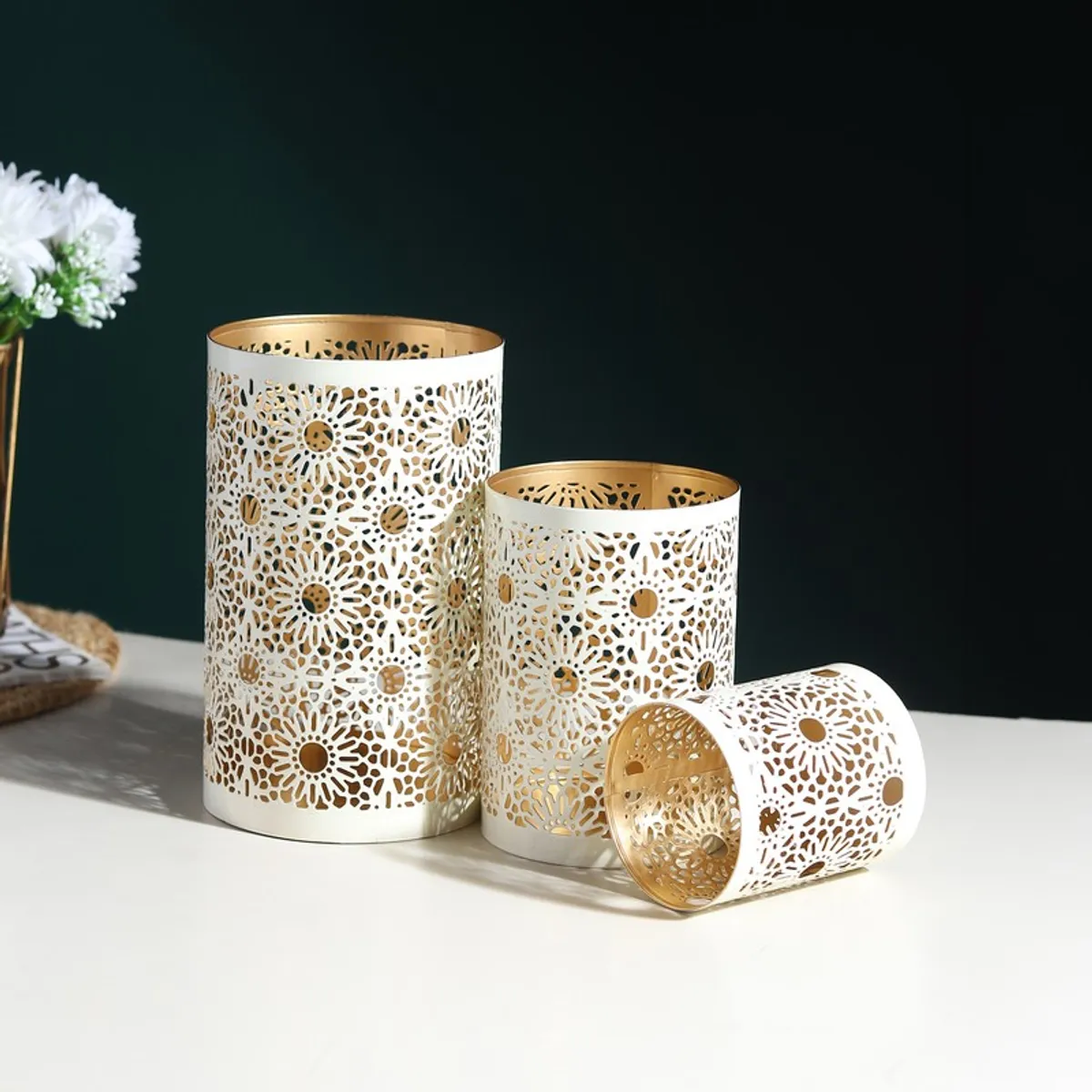 Three white floral lattice candle holders arranged on a table, with one lying on its side