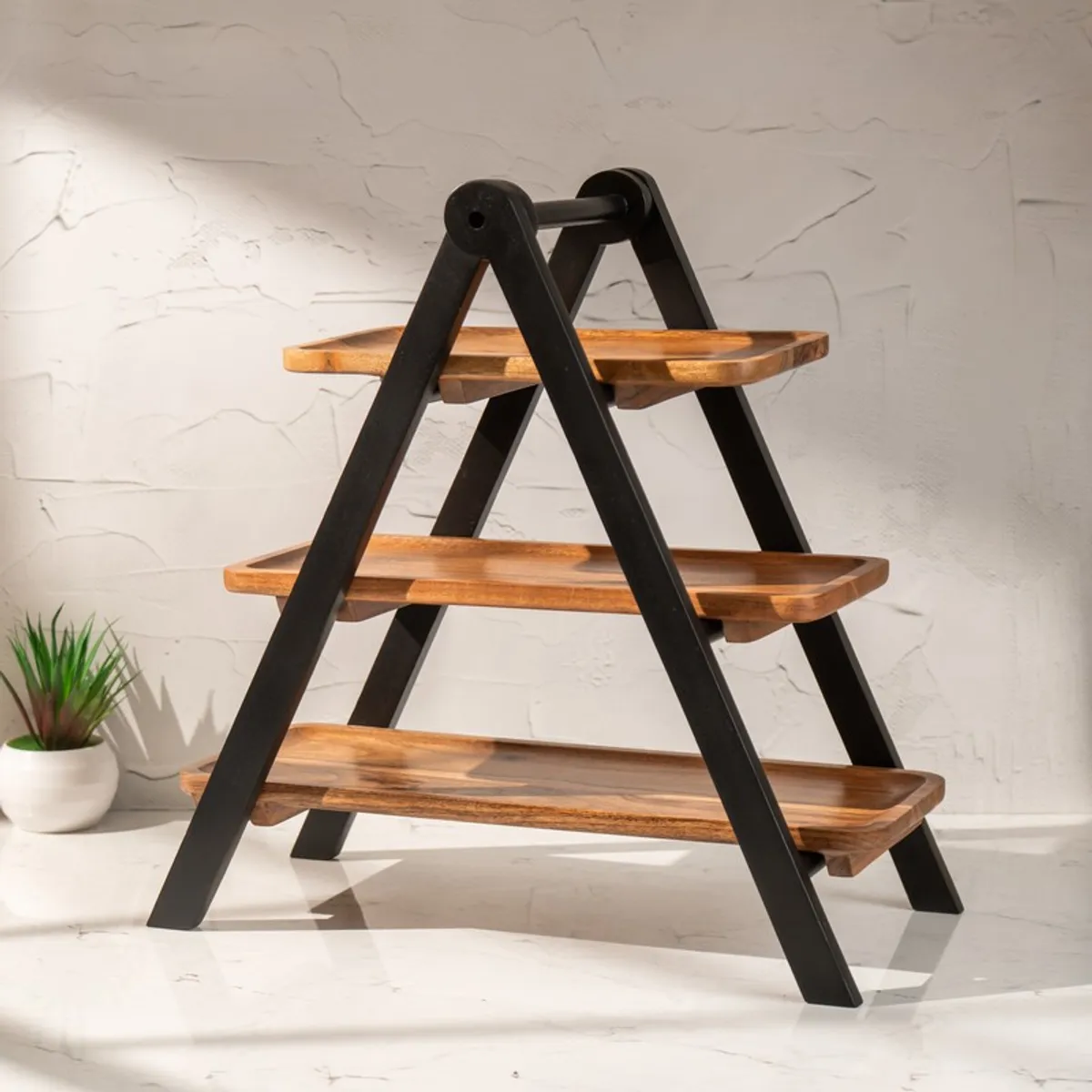 Three-tier wooden serving stand shown against a textured white wall