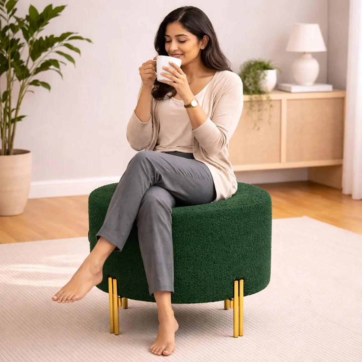 Person seated on a green round bouclé ottoman with gold legs