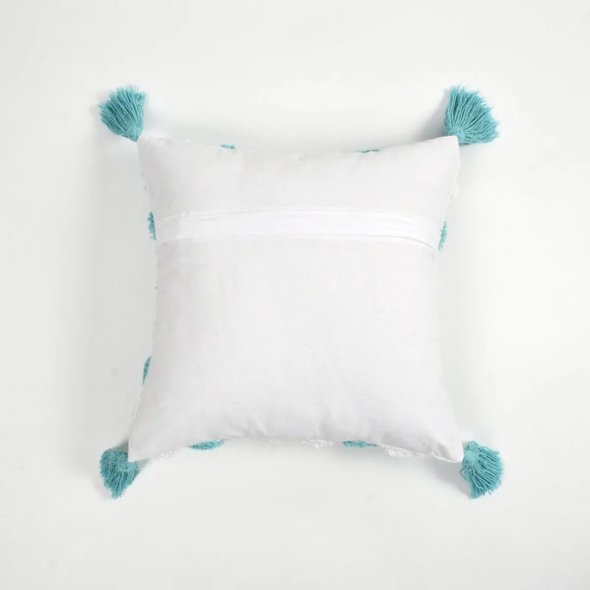 Back view of a white cushion cover showing its zip closure and tassels