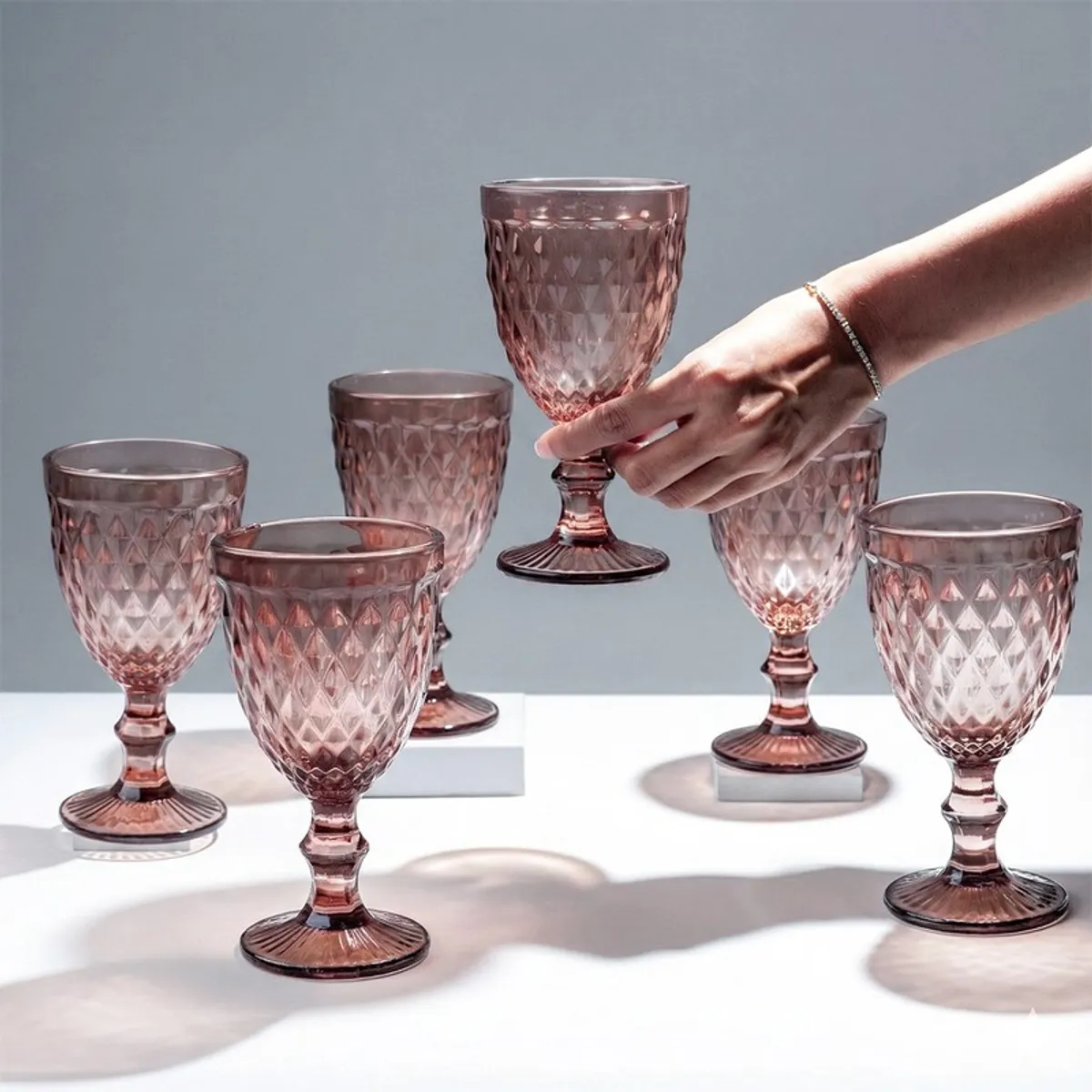 Hand holding a pink textured stemmed wine glass with others displayed
