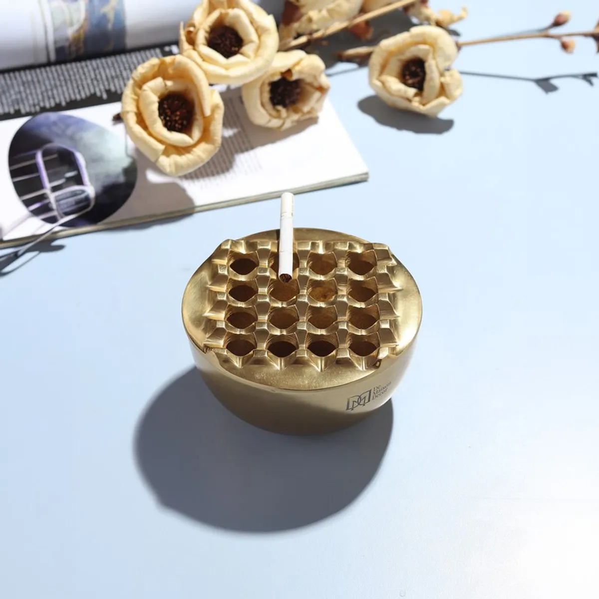 Gold ash tray shown with a cigarette resting in its sculpted top