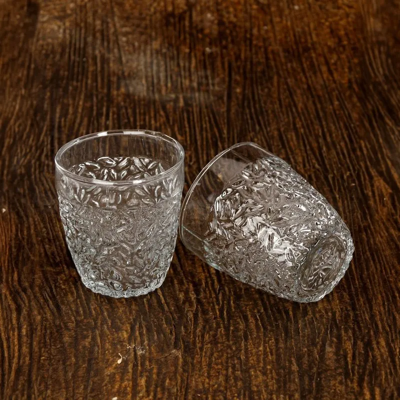 Two clear textured drinking glasses on a dark wooden surface