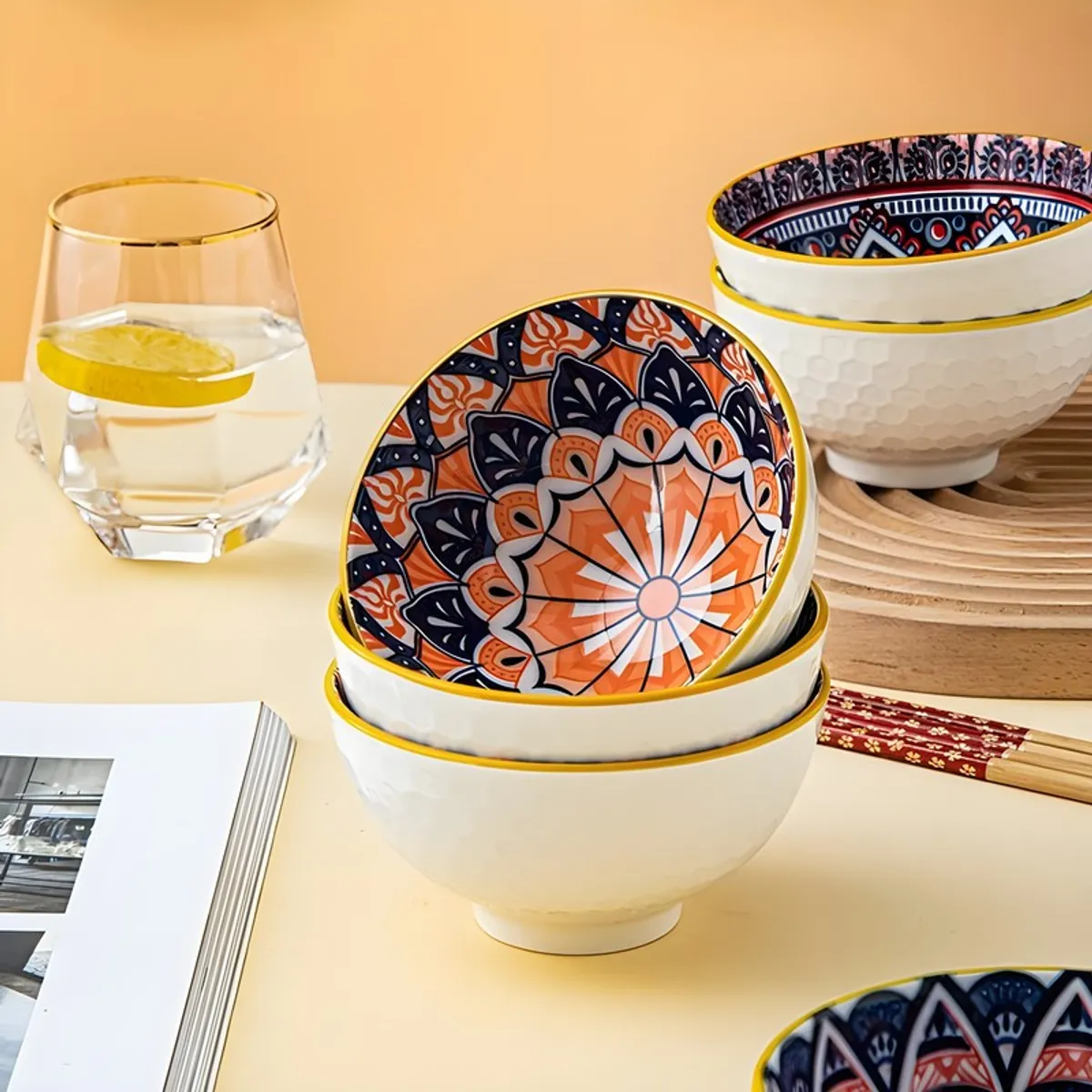 Stacked ceramic bowls with vibrant orange and blue mandala patterns on a dining table.