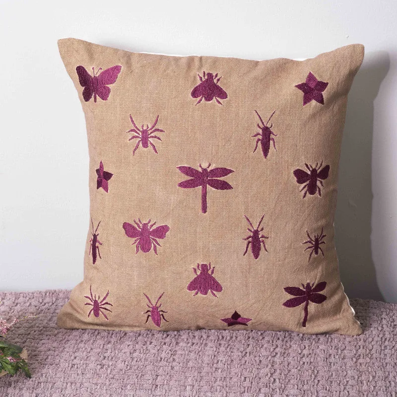 Close view of a beige cushion cover with pink dragonfly and insect motifs.