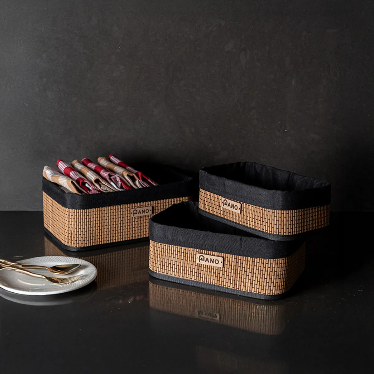 Set of three rectangular black and natural woven storage baskets on a dark surface