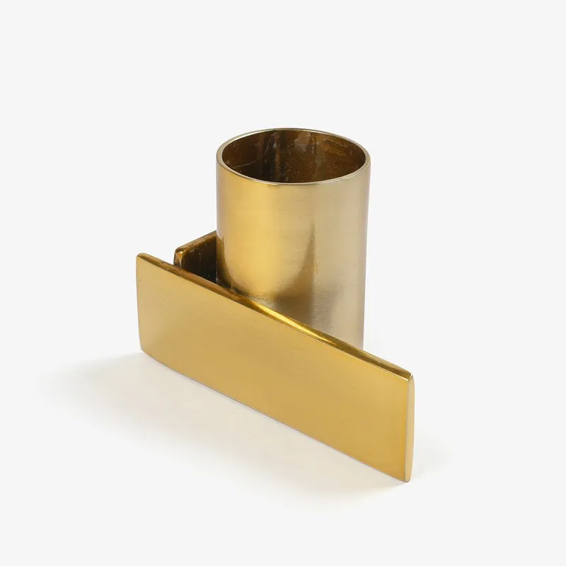 Close view of a gold candle holder with a cylindrical cup and flat geometric plate