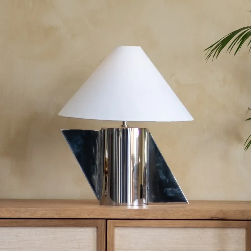 White conical shade table lamp with angular silver base on wooden surface