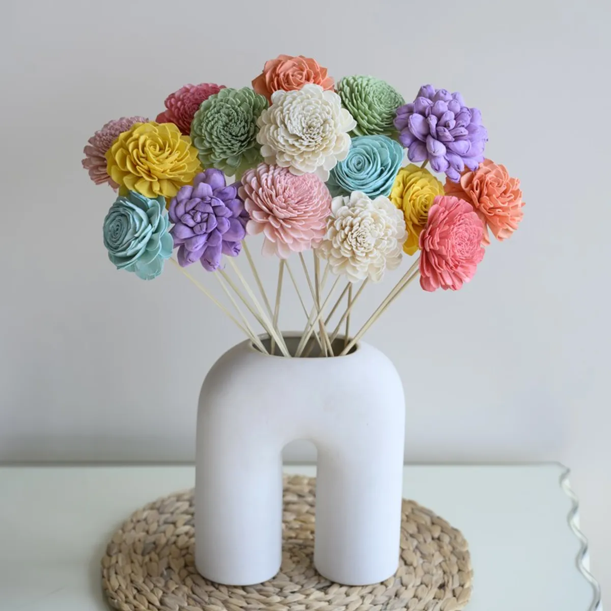 Multicolour flower sticks arranged in a rounded white vase on a mat